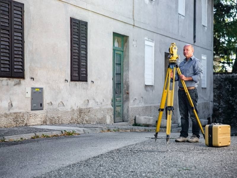 Land surveyor locating property boundary markers before fence or garage construction.
