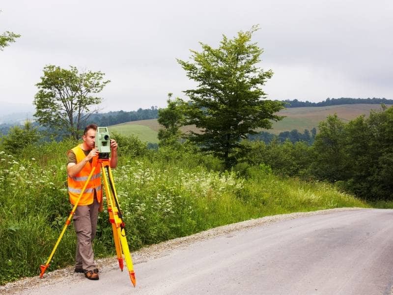 Land surveyor measuring elevation on rolling terrain to support construction planning on a sloped property.