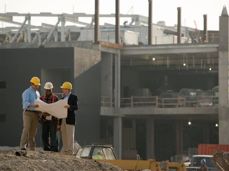 Engineers reviewing construction plans at a development site, illustrating how topographic survey data supports safe design, foundation planning, and site development on uneven terrain.