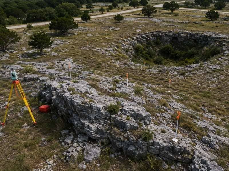 Exposed limestone ledges and a closed ground depression mapped with survey stakes across an uneven development site.